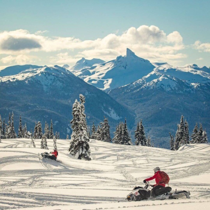 Two people on snowmobiles exploring terrain at Whistler