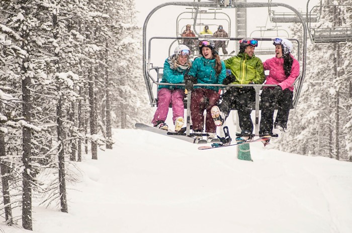 Skiers on chairlift enjoy early season powder at Panorama