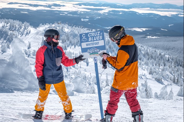 Pair of snowboarders point to Cruz the Blues sign at Big White