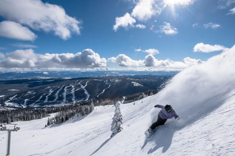 A photo of a snowboarder going down a snow-covered hill on a sunny, winter day.