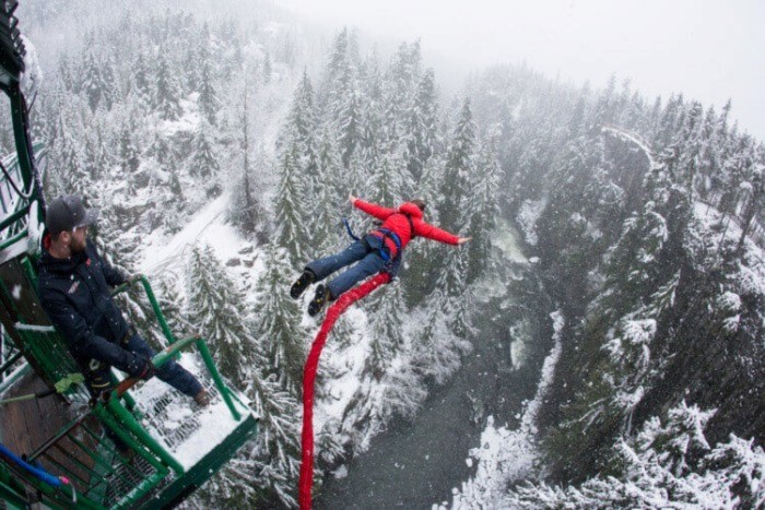 Man in red winter coat bungee jumping over the Whistler forest in winter