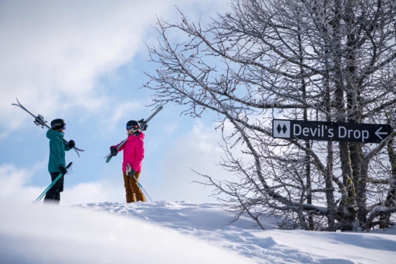 Two skiers at Panorama next to a sign that says Devil's Drop.