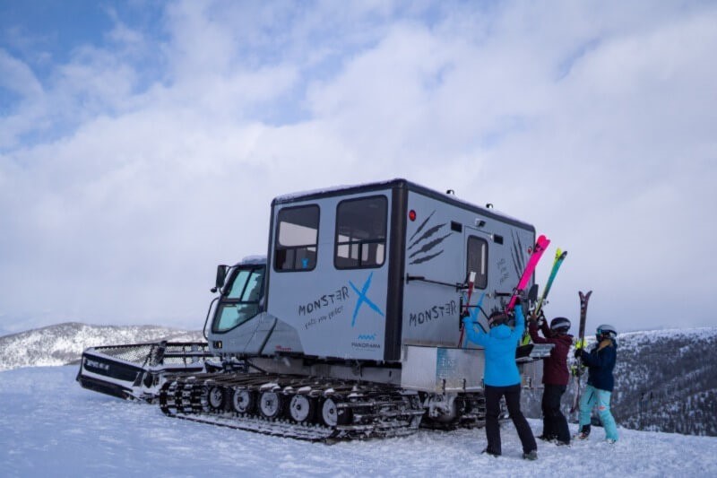 Three women adding their skis to the back of a snowcat at Panorama.