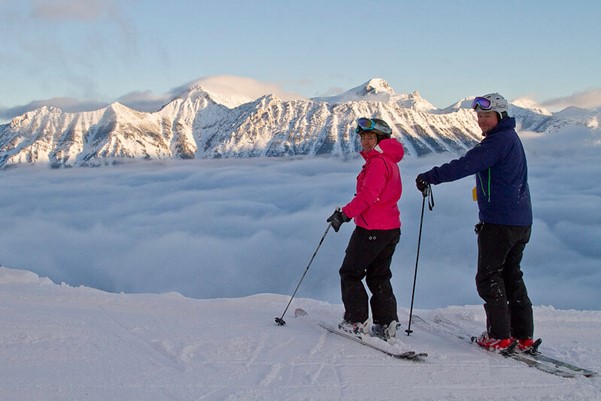 Two people standing at the top of a mountain above the clouds