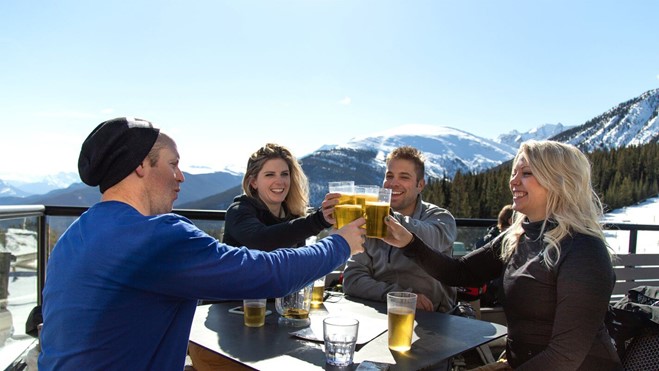 Four people with their beers together over a table to cheers