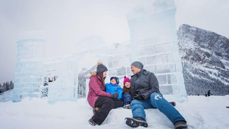 A photo of a family of four including a mom, dad, and two children sitting in front of an ice sculpture in Banff.