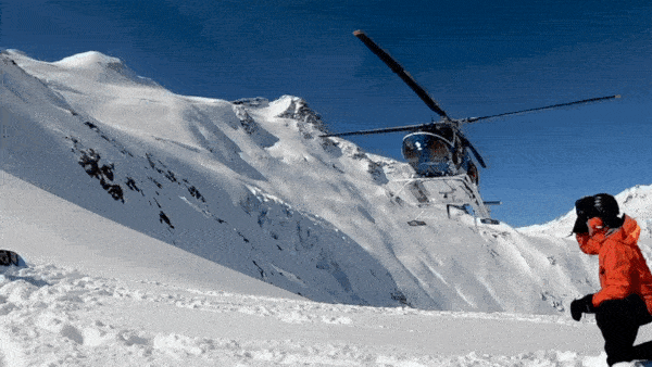 A gif of a helicopter landing in the snow next to a person in a red jacket.
