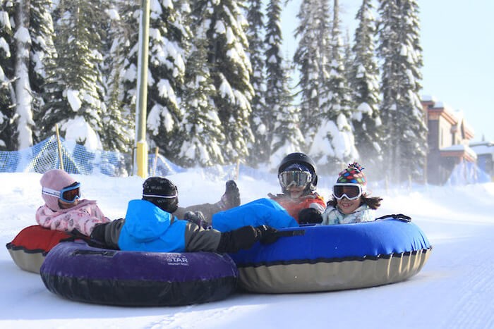 A family of four on snow tubes riding down a slope in winter