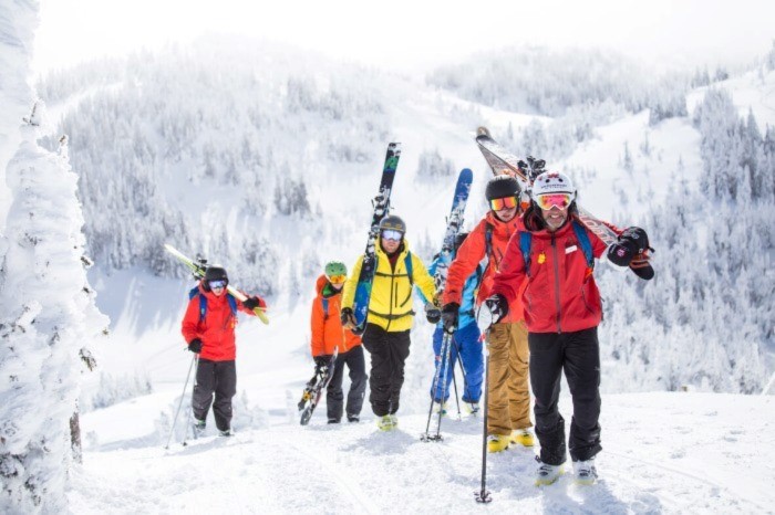 Group of six skiers and snowboarders walking up a snowy hill