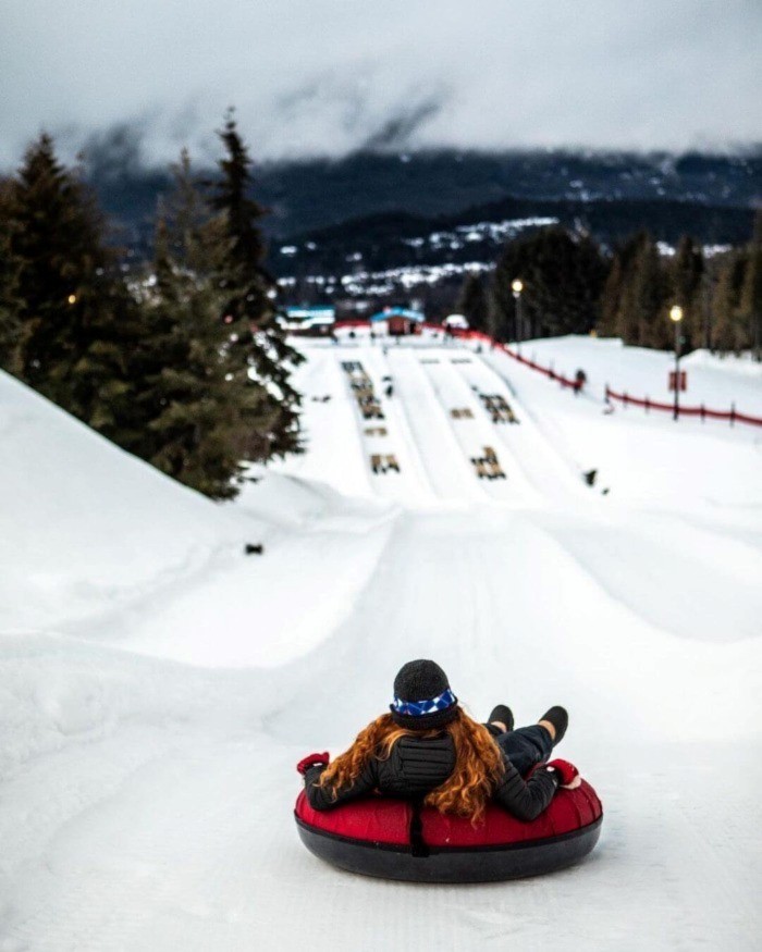 A young woman with long red hair sliding down a hill in a tube