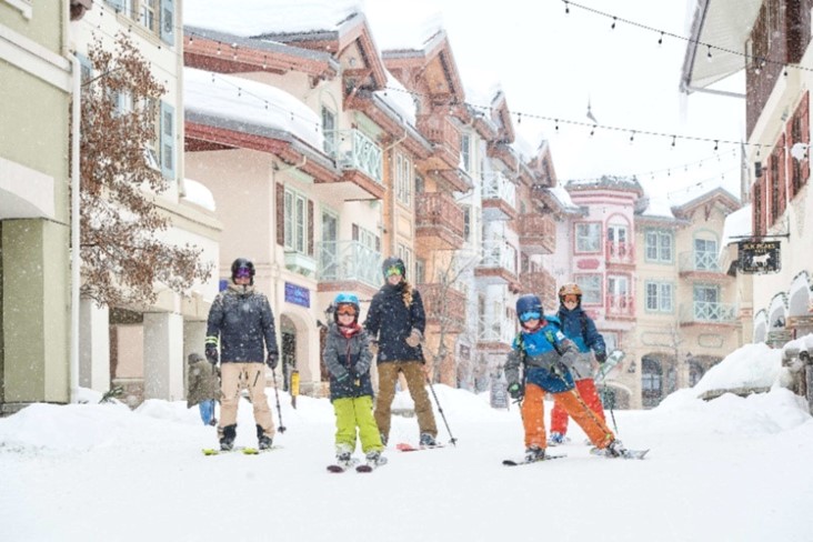 Two parents with three children skiing through the village at Sun Peaks while it snows.